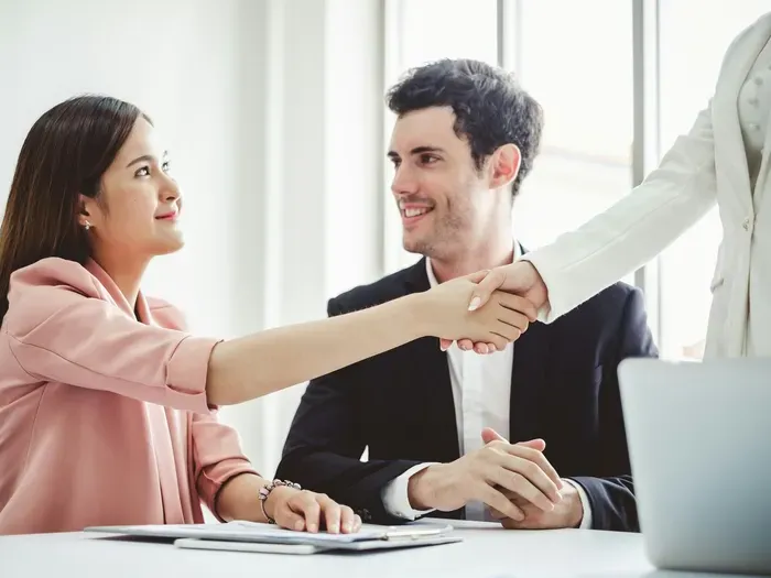 Two professionals smiling and shaking hands across a desk during a successful business meeting on localservicenet.net